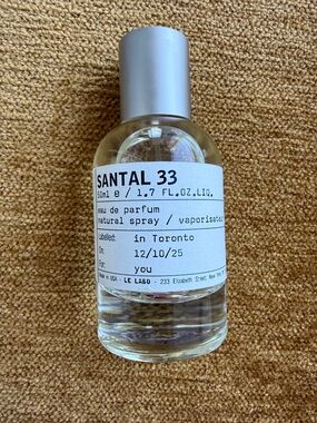 Le Labo Santal 33 - Clear Glass Bottle with Silver Cap on Tan Surface